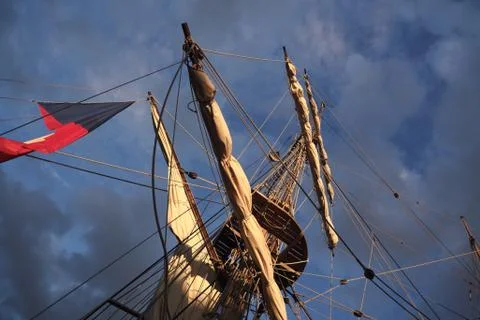 Tall ship masts and rigging silhouetted against a dramatic sky at sunset Stock Photos