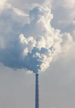 A tall smoke stack is spewing smoke into the sky Stock Photos