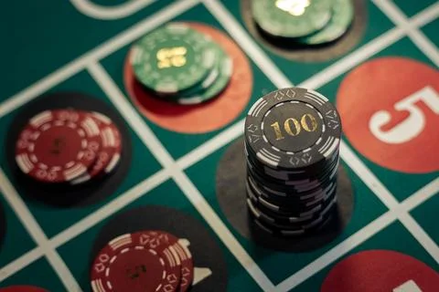 Tall stack of black one hundred casino chips on green roulette table. Stock Photos