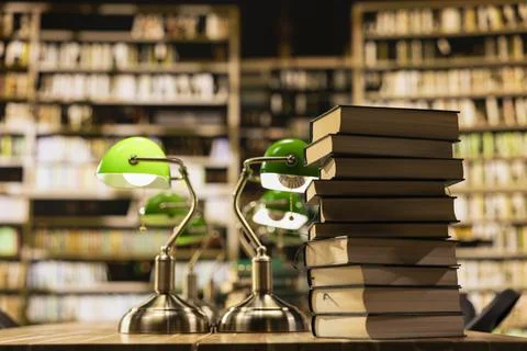 Tall stack of books on library table with green lamps against bookshelves Stock Photos