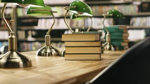 Tall stack of books on library table with green lamps against bookshelves Stock Photos