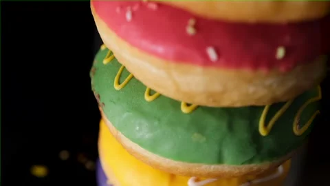 Tall stack of yummy donuts with different color frosting and sprinkles on black Stock Footage 254662784