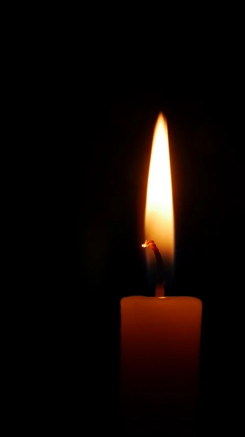 A tall vertical candle flame flickers upward against black background expressing Vídeo Stock 325381561
