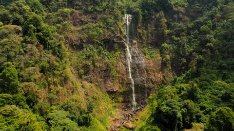 Tall waterfall cascading down rocky cliff surrounded by dense jungle in Costa Stock Footage 327791936
