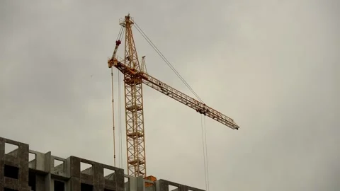 Tall yellow construction crane operating above concrete building framework Stock Footage 348026368