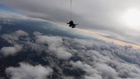 Tandem skydiving jump in the cloudy sky with the sun in the background - Stock Footage 241559926
