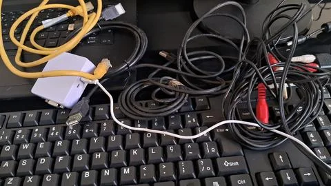 Tangled computer cables on a keyboard. Messy electronic wires and tech Stock Photos