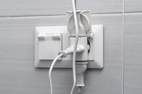 Tangled plugs crowd a wall socket, capturing a close view of overloaded Stock Photos
