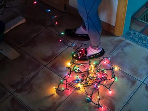 Tangled string of Christmas lights at the bottom at a woman's feet while Stock Photos