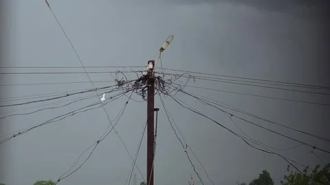 Tangled utility wires web outward from a central pole against a dark, stormy sky 库存影片 337350361