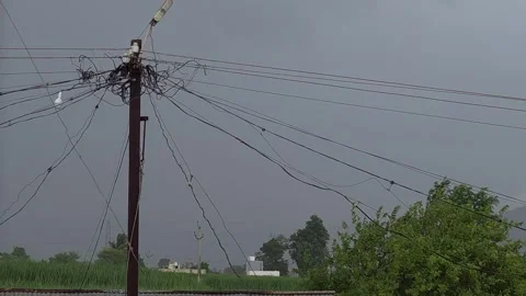 Tangled wires clutter a rural utility pole beneath a dark, stormy sky. Green fie Video stock 337350364