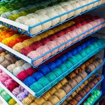 Tangles of multi-colored threads and yarn lie in rows on a metal stand Stock Photos