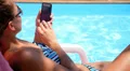 Tanned Girl in Bikini Lying on a Sun Lounger by the Pool with a SmartPhone. HD Footage