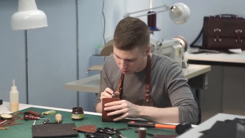 A tanner in an apron paints the ends of a leather wallet. Master in the workshop Stock Footage 104926923