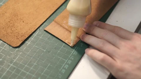 A tanner makes a brown leather wallet. Apply glue to the workpiece. Squeezes out Stock Footage 104925642