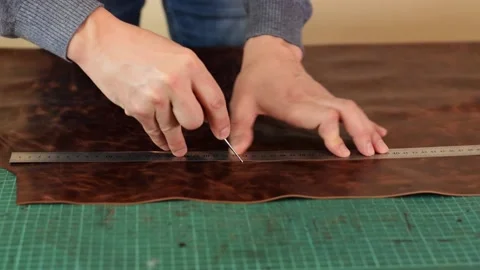 Tanner making markings on a sheet of brown leather with a ruler and awl. Stock Footage 150477582