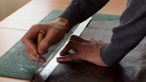 Tanner making markings on a sheet of brown leather with a ruler and awl. Stock Footage 150477693
