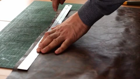 Tanner making markings on a sheet of brown leather with a ruler and awl Stock Footage 150477749
