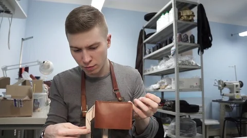 Tanner manually stitches a leather product. Man sews a brown leather wallet Stock Footage 104927404