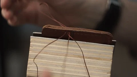 Tanner manually stitches a leather product. Man sews a brown leather wallet Stock Footage 104927464