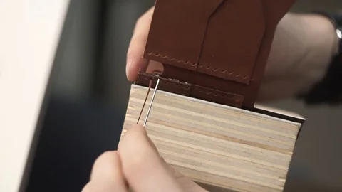 Tanner manually stitches a leather product. Man sews a brown leather wallet Stock Footage 104927509