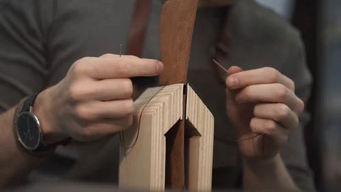 Tanner manually stitches a leather product. Man sews a brown leather wallet Stock Footage 104927567