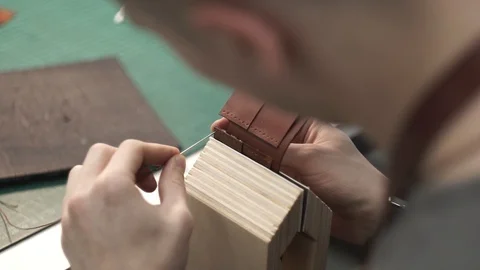 Tanner manually stitches a leather product. Man sews a brown leather wallet Stock Footage 104927630