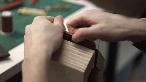 Tanner manually stitches a leather product. Man sews a brown leather wallet Stock Footage 104928016