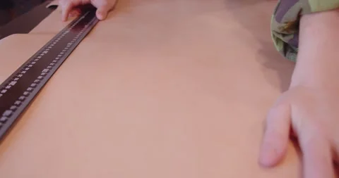 A tanner measures a large sheet of leather with a ruler for making a bag Stock Footage 148383974