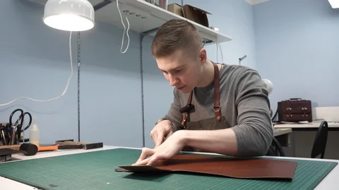 A tanner in the workshop cuts the skin. Making a purse of brown leather. Young Stock Footage 104926003