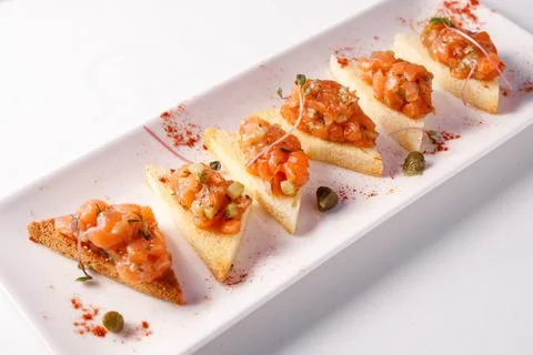 Tapas with fish on a white plate. Small sandwiches. Stock Photos