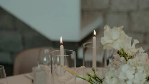 Taper candles burning beside white flowers on a table Stock Footage 346112574