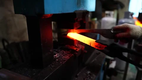 Tapering a glowing steel bar under a power hammer while gas cylinders stand in Stock Footage 343370481
