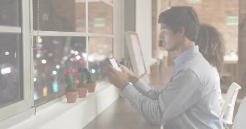 Tapping blue-shirt man using phone at desk by window, with screens, cacti and Stock Photos