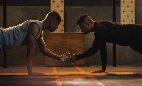 Tapping into an intense workout. two young men doing pushups together in a gym. Stock Photos