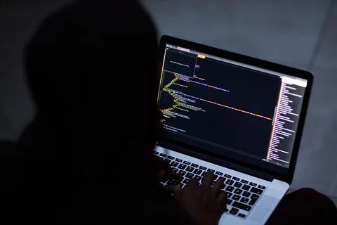 Tapping into the main frame. an unrecognisable hacker using a laptop in the dark Stock Photos