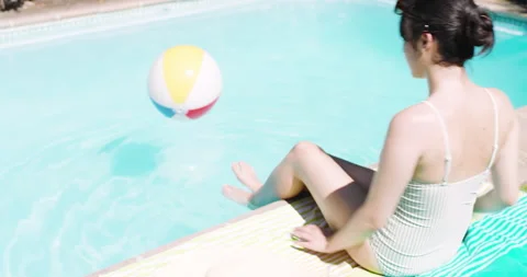 Tapping phone, noticing beach ball bouncing, Asian woman dipping into home pool Stock Footage 310368694
