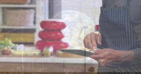 Tapping stylus on tablet while chef wearing apron at kitchen counter, with globe Fotos de archivo