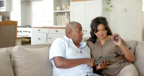 Tapping tablet, senior couple sitting on sofa and examining black remote, Stock Footage 339592172