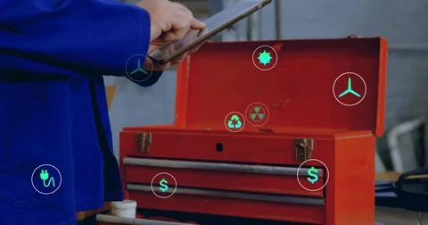 Tapping tech in blue coverall holding tablet at workbench, showing red toolbox Stock Photos