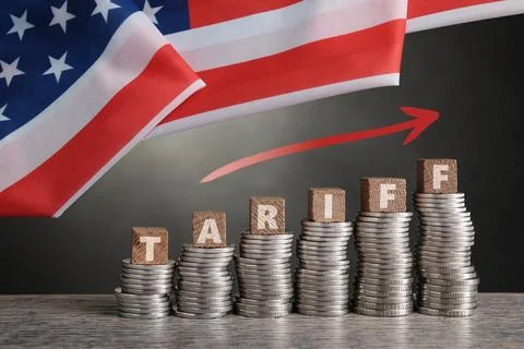 Tariff increase. Stacks of coins with cubes on table under flag of USA Stock Photos