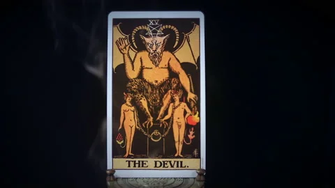 A tarot Devil card sits on a brass stand as smoke rises around it. The Stock Footage 143061295
