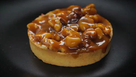 Tart with nuts and caramel rotating on black plate Stock Footage 99252280