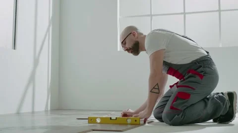 Taskmaster with glasses checks parquet floor level in room Stock Footage 150101057