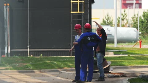 Taskmaster talks to builders near large plant building Stock Footage 221168460