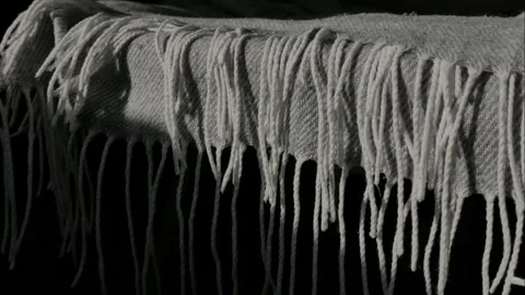 The tassels ends of a blanket hanging over the edge of a chair or bed. Stock Footage 332572001