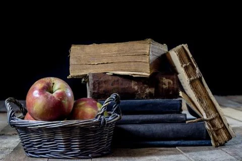 Tasty apples in basket on kitchen table. Old books lie next to apples in a ga Stock Photos