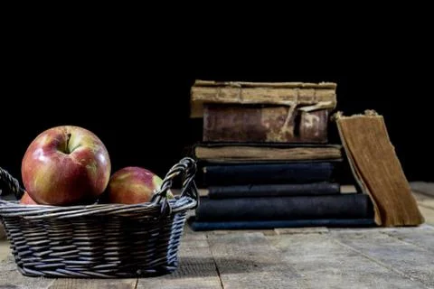 Tasty apples in basket on kitchen table. Old books lie next to apples in a ga Stock Photos
