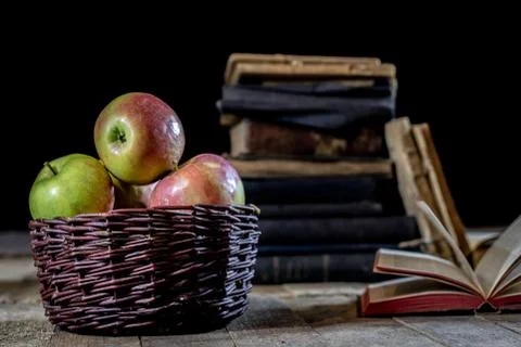 Tasty apples in basket on kitchen table. Old books lie next to apples in a ga Stock Photos
