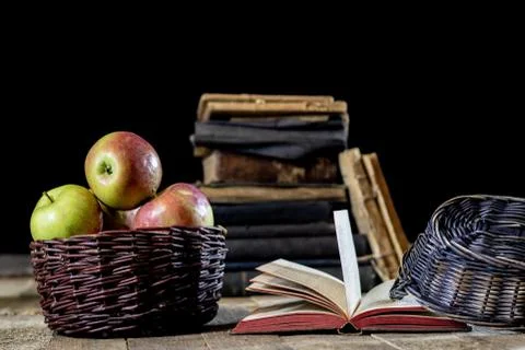 Tasty apples in basket on kitchen table. Old books lie next to apples in a ga Stock Photos
